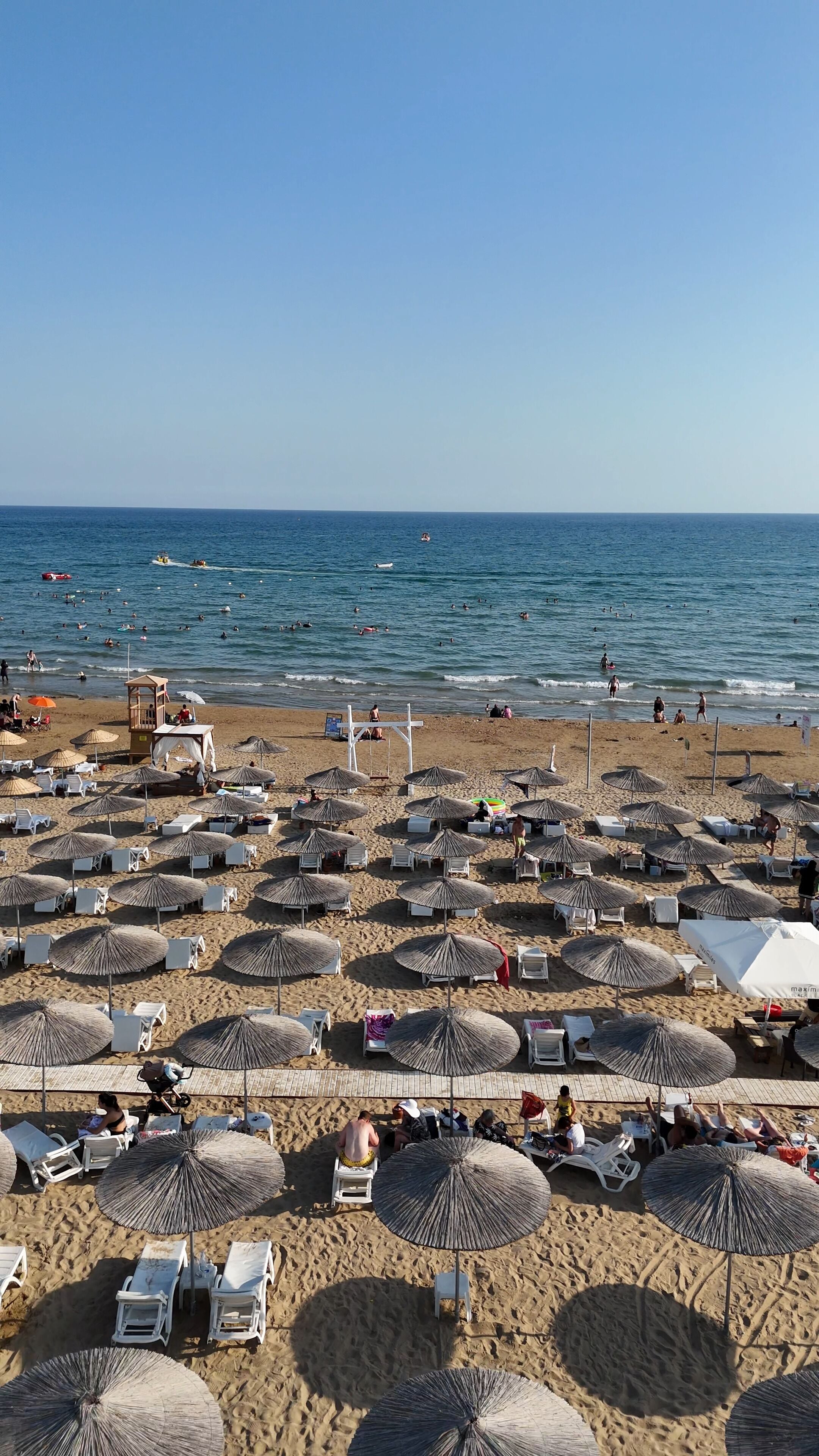 A beach with numerous umbrellas and lounge chairs, a lifeguard tower, and the ocean in the background.