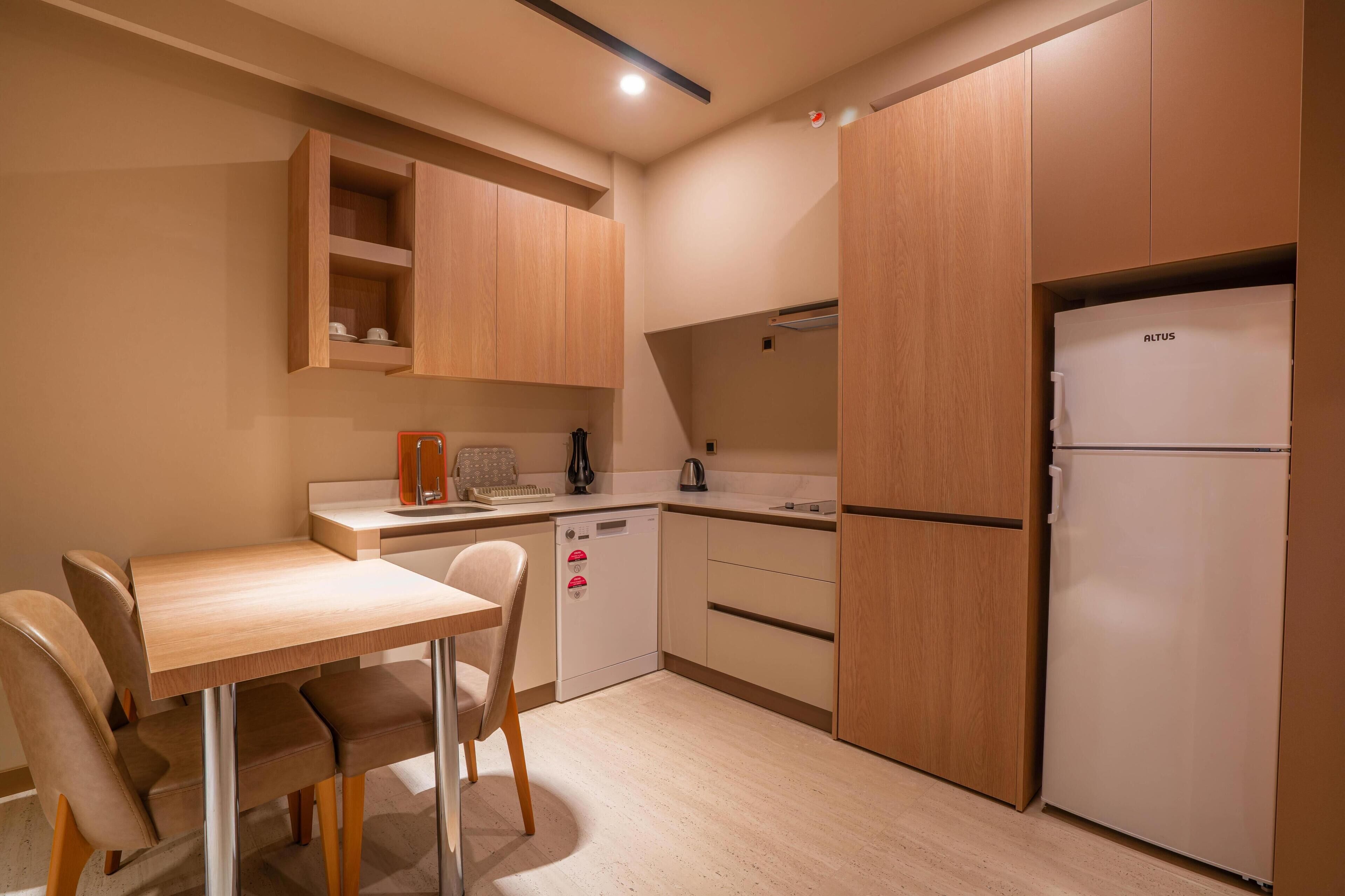 A compact kitchen with a wooden table, chairs, a dishwasher, and a refrigerator.