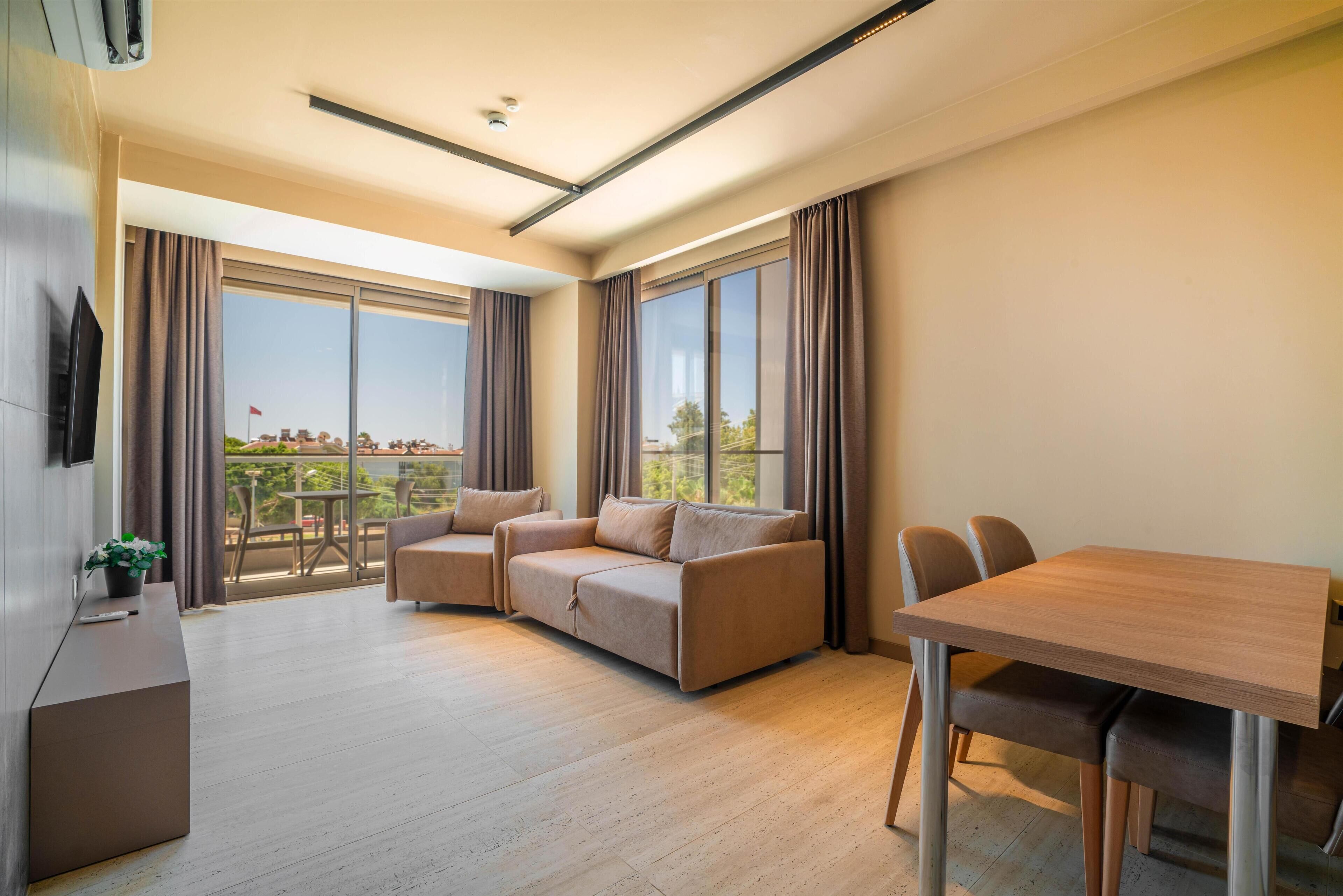 A modern living room with a sofa set, a dining table, and a balcony with a view.