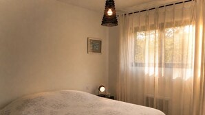 A bedroom with a bed, a bedside lamp, a framed picture on the wall, and sheer curtains.