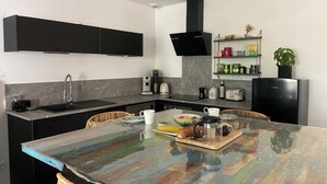 A modern kitchen with a central island, black cabinets, a built-in stove, and a coffee maker.