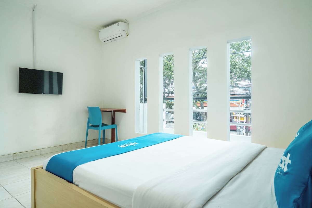 A hotel room with a bed, a desk, a chair, and a TV mounted on the wall.