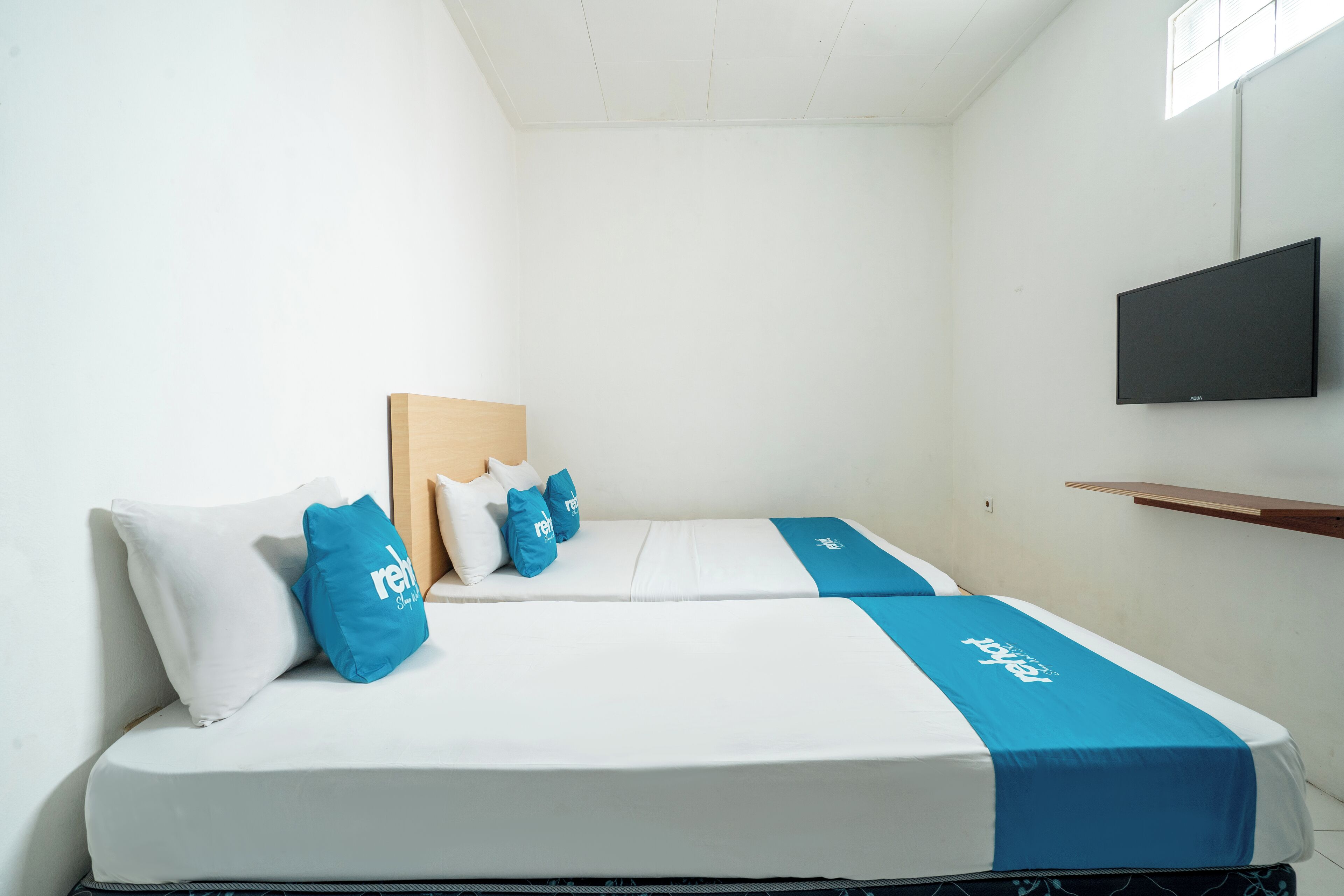 Una habitación de hotel con cama, almohadas, televisor y repisa.