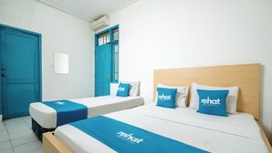 A hotel room with two single beds, each with a blue bedspread and matching pillows, and a larger bed with a wooden headboard. - Rehat at Paskal Pelangi (Bandung)
