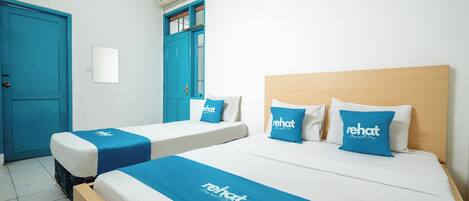Une chambre d’hôtel avec deux lits simples, chacun recouvert d’une couvre-lit bleue et agrémenté d’oreillers assortis, ainsi qu’un lit plus grand doté d’une tête de lit en bois.