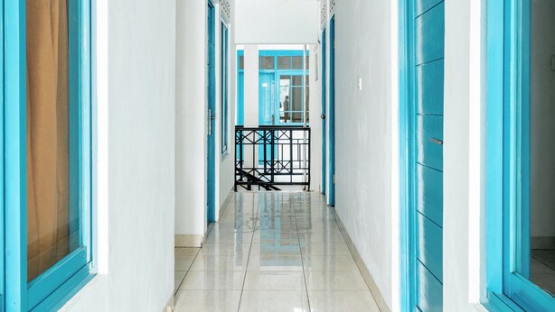A hallway with blue doors and white walls, leading to a staircase with a black railing. - Rehat at Paskal Pelangi (Bandung)