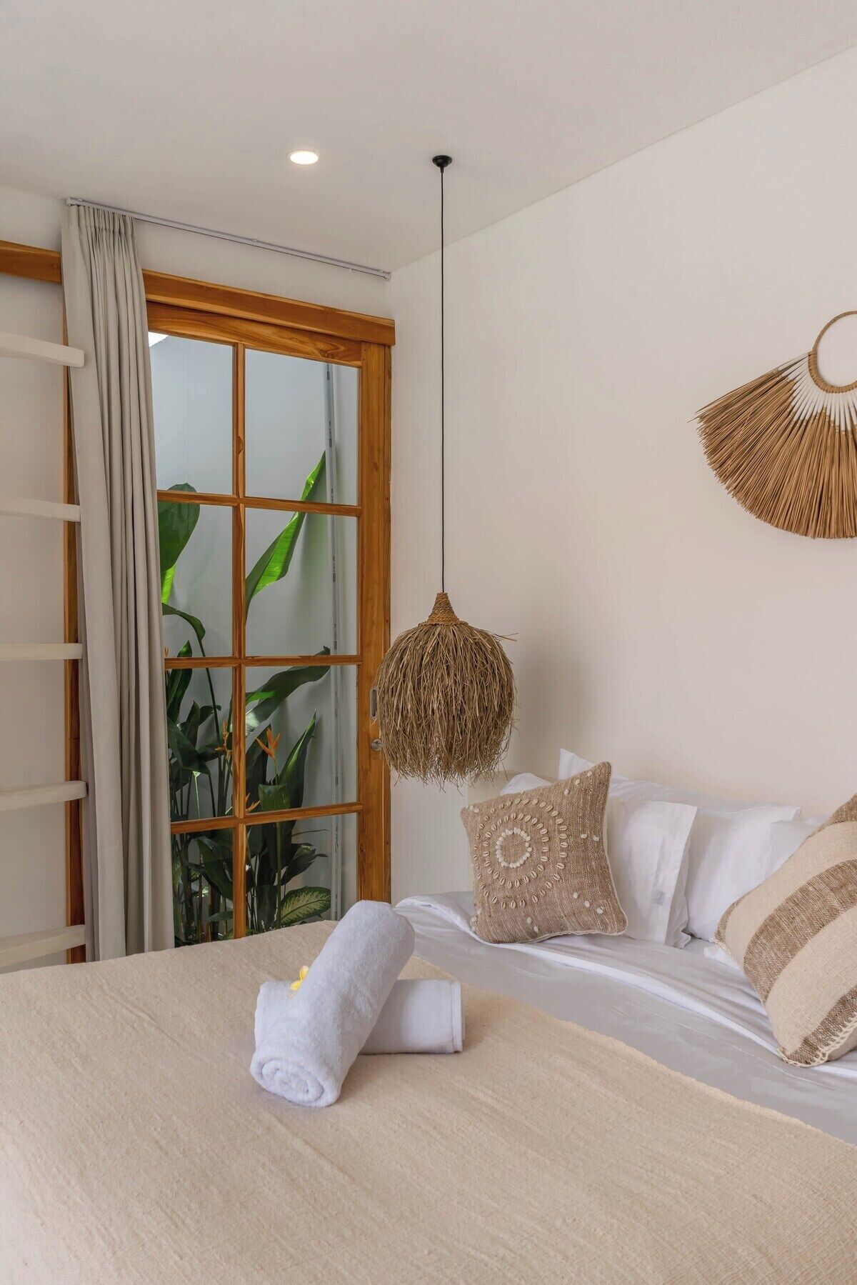 Une chambre avec un lit, un luminaire suspendu en fibres tressées et une vue sur la verdure par la fenêtre.