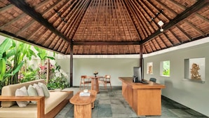 A reception area with a wooden desk, a sofa, and a coffee table. There are chairs around the table, and the area is surrounded by plants. - Mayaloka Villas Ubud (Ubud)