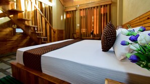 Habitación de hotel con escalera de madera, cama con ropa blanca, almohada marrón y un ramo de flores.