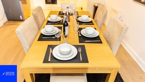 Une table à manger dressée avec de l’argenterie blanche, des couverts et des verres, et une bouteille de champagne placée au centre.