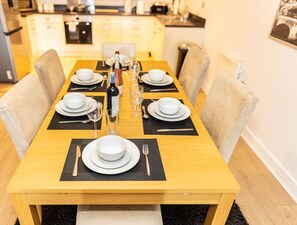 A dining table set with white plates, cutlery, and glasses, with a bottle of champagne in the center. - 2ndHomeStays I Birmingham | Ensuite | Parking&WiFi (West Midlands)
