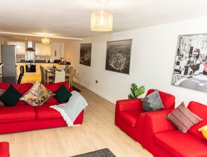 A modern living room with a red sofa set, a dining area, and a kitchen in the background. - 2ndHomeStays I Birmingham | Ensuite | Parking&WiFi (West Midlands)