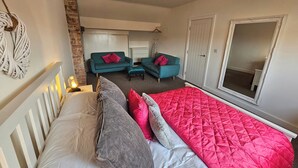 Ein Schlafzimmer mit einem Bett, zwei Sofas, einem Spiegel und einer Pendelleuchte.