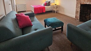 Ein gemütliches Wohnzimmer mit Kamin, einem Bett mit roter Bettwäsche und einem blauen Sofa.