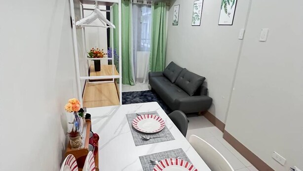 A modern living room with a dining area, grey sofa, and a white table set for two. - Unistay Shore3 Poolview w bal (Pasay)