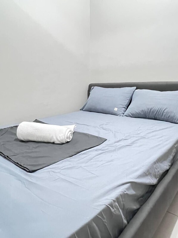 Un lit simple avec une literie et des oreillers gris, une serviette blanche posée sur le lit et une tête de lit grise.