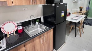 A modern kitchen with wooden cabinets, a black refrigerator, a microwave, and a sink. There is a dining area with a table and chairs. - Unistay Shore3 Poolview w bal (Pasay)