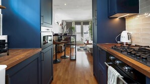 A modern kitchen with dark cabinetry, a wooden countertop, and a gas stove. - Stylish Balcony Apartment by London Fields - Pass the Keys (London)