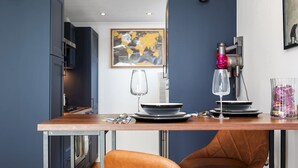 A modern kitchen with a wooden countertop, two brown leather chairs, a coffee machine, and a framed abstract painting on the wall. - Stylish Balcony Apartment by London Fields - Pass the Keys (London)