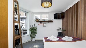A modern hotel room with a large bed, a wooden wardrobe, a small window, a TV, and a ceiling light. - Stylish Balcony Apartment by London Fields - Pass the Keys (London)
