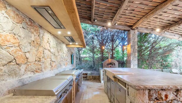 A stone-clad outdoor kitchen with a pizza oven, built-in bar, and stone walls.
