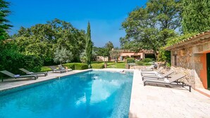 A swimming pool with lounge chairs, surrounded by greenery and stone buildings.