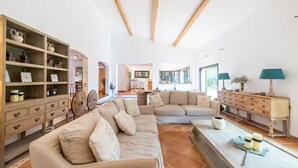 A spacious living room with a large L-shaped sectional sofa, wooden shelving with decorative items, and a dining area with a table and chairs.