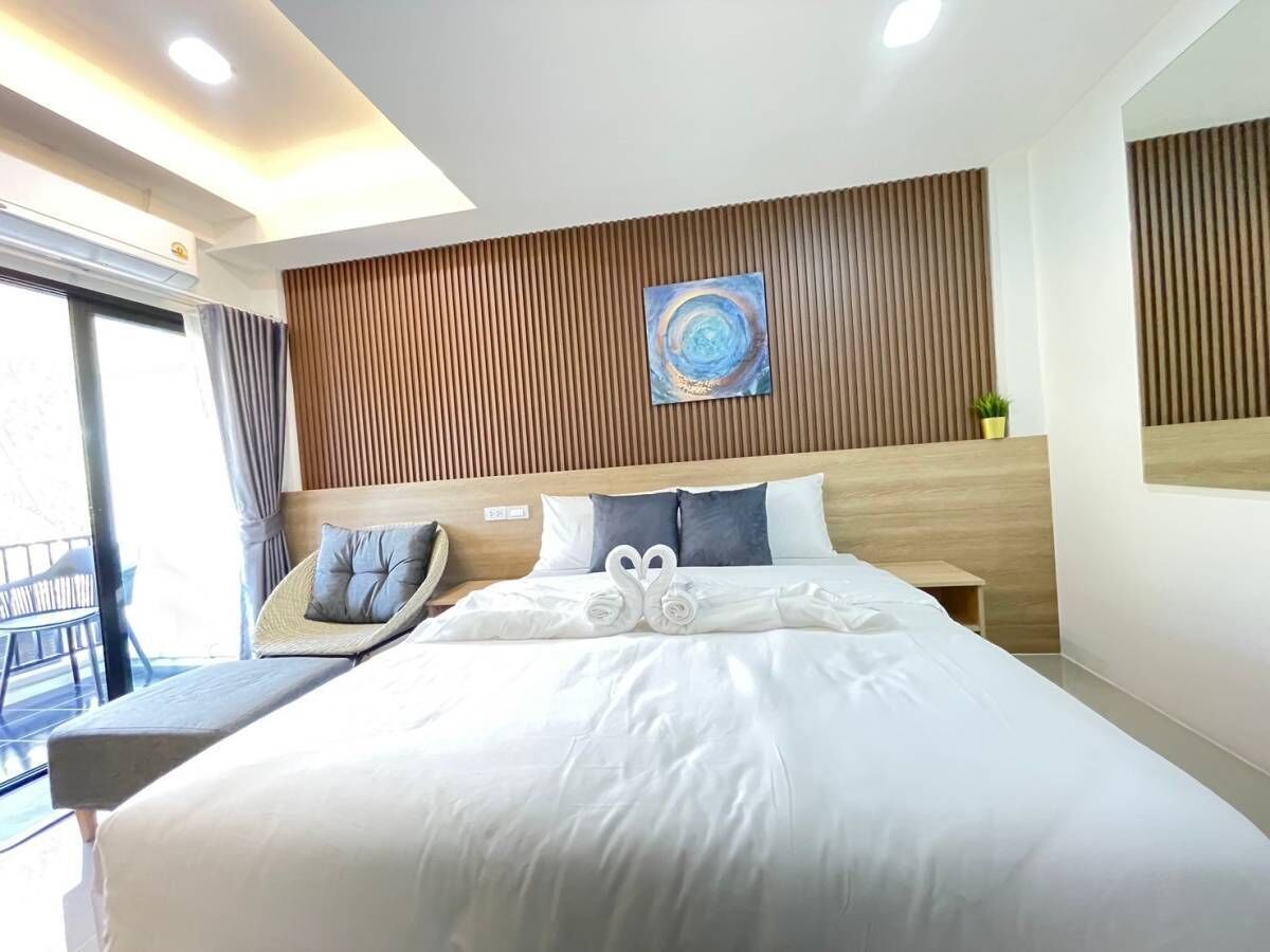 Une chambre d’hôtel moderne avec un grand lit, une tête de lit en bois, un tableau et un balcon avec une chaise.