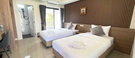 A hotel room with two beds, a desk, and a shower area.