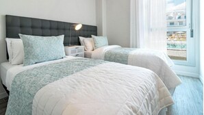 Habitación de hotel con dos camas, una moderna cabecera, una lámpara de noche y vistas a una piscina a través de un amplio ventanal.