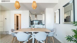 Un comedor moderno con una mesa de madera y cuatro sillas, una cocina al fondo y un espejo grande en la pared.