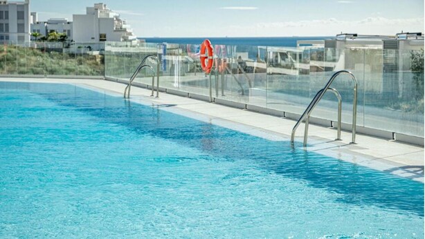 Una piscina con agua azul cristalina, barandillas metálicas y un flotador en el borde.