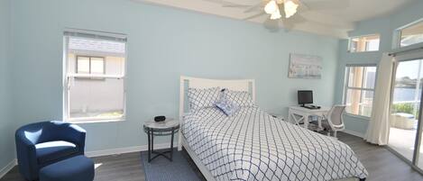 Ein Schlafzimmer mit Bett, Schreibtisch, Stuhl, Deckenventilator und Fenster.