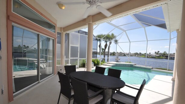 Uma área externa coberta com piscina, mesa de jantar e cadeiras.
