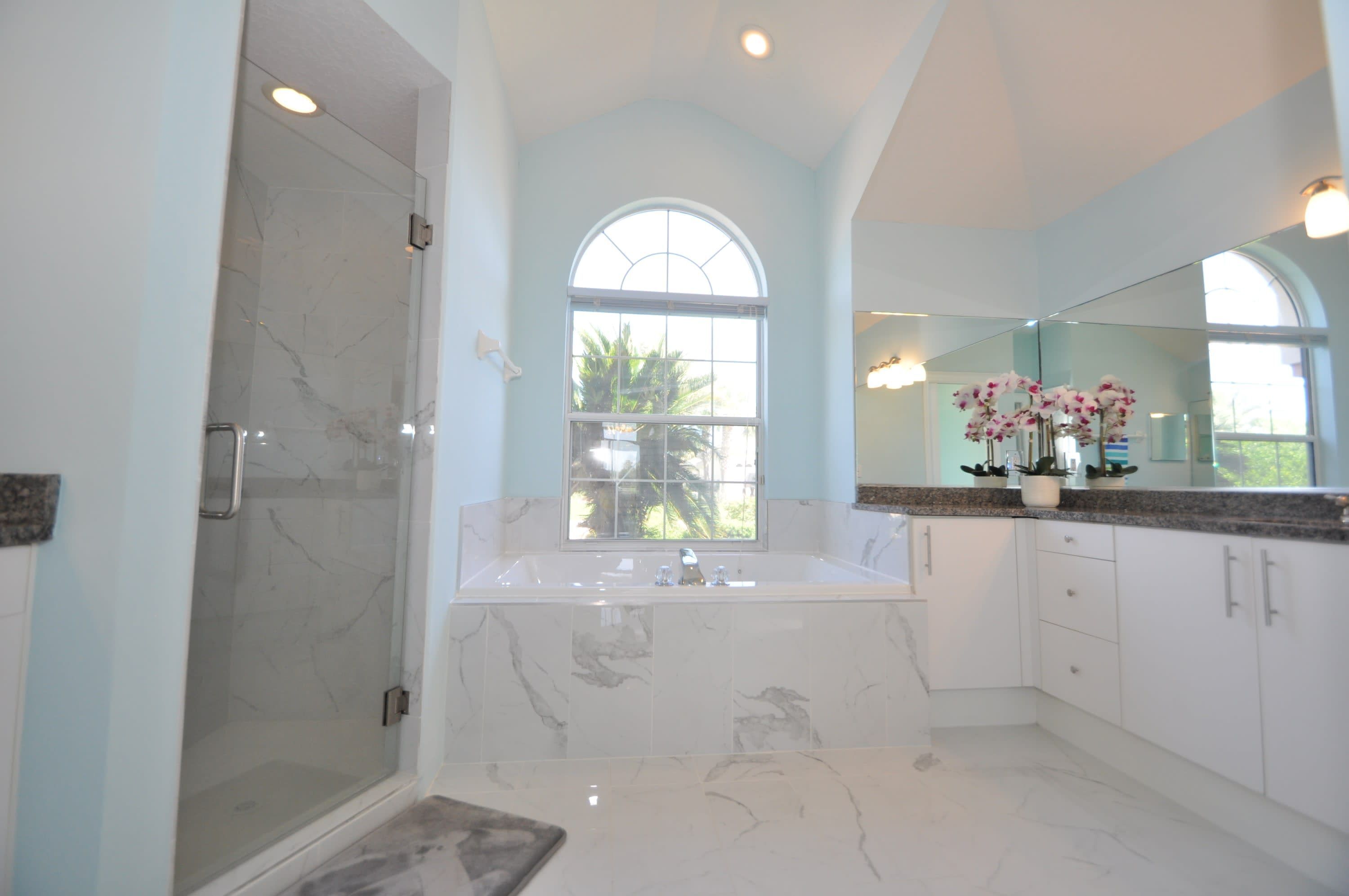 A modern bathroom with a glass-enclosed shower, a large bathtub, and a vanity with a mirror.