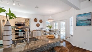 A modern kitchen with granite countertops, a large island, and a dining area with white chairs. - Bring Your Boat Heated Pool spa Dock Beach (Palm Coast)