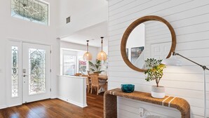 A spacious room with wooden flooring, a round mirror on the wall, a dining area with chairs and a table, and a large window with stained glass. - Bring Your Boat Heated Pool spa Dock Beach (Palm Coast)