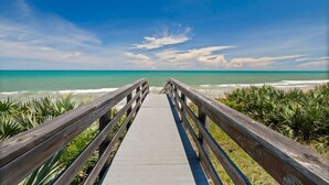 Une promenade en bois mène à une plage où l’eau est d’un bleu turquoise et le ciel, d’un bleu éclatant.