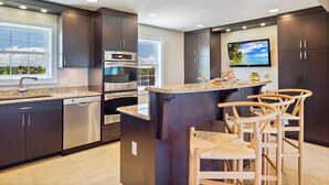 Une cuisine moderne avec des meubles de couleur sombre, des appareils en acier inoxydable, un comptoir en granit et un coin bar agrémenté de chaises en osier.