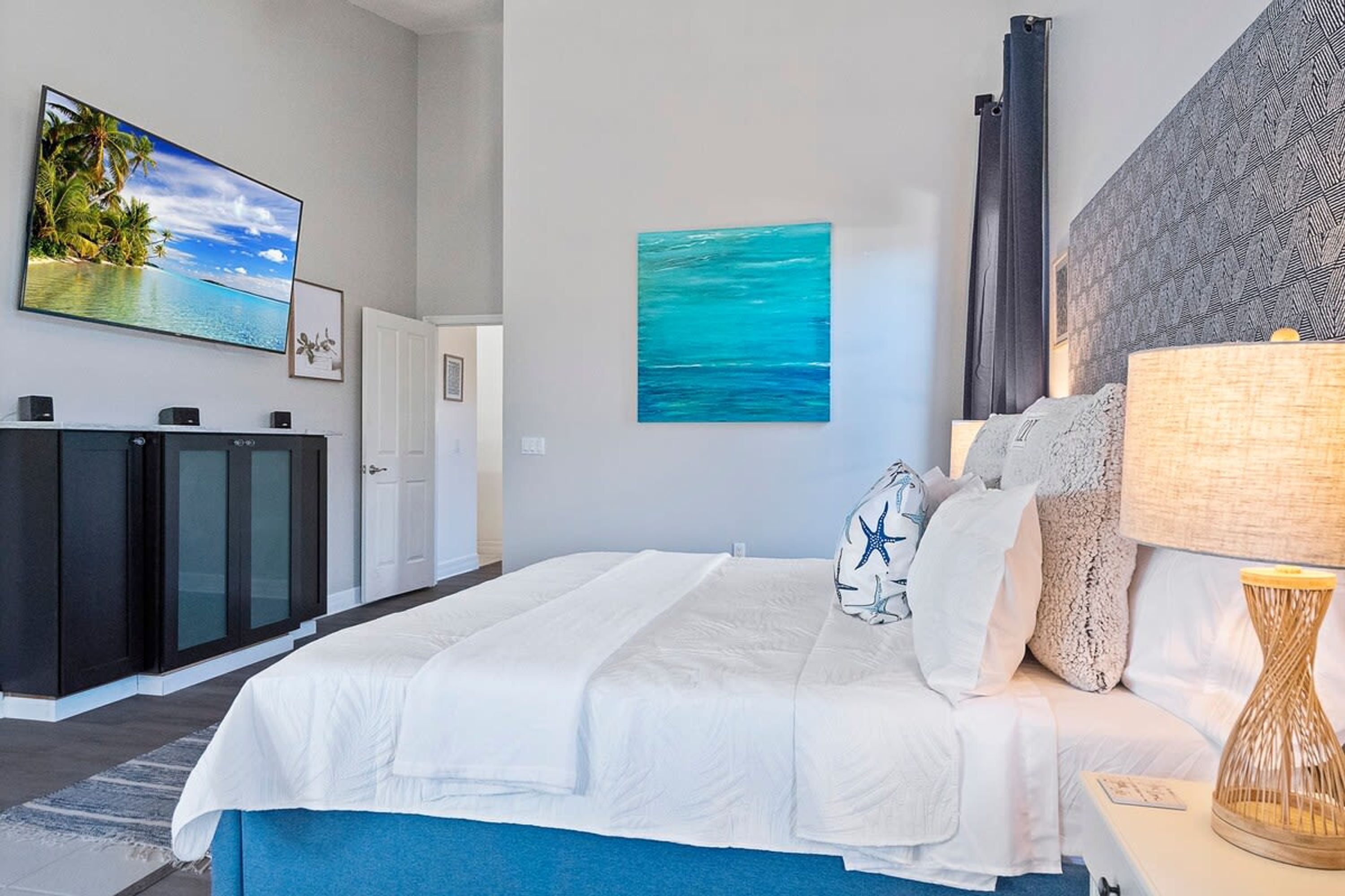 A bedroom with a bed, a TV, a painting, and a lamp.