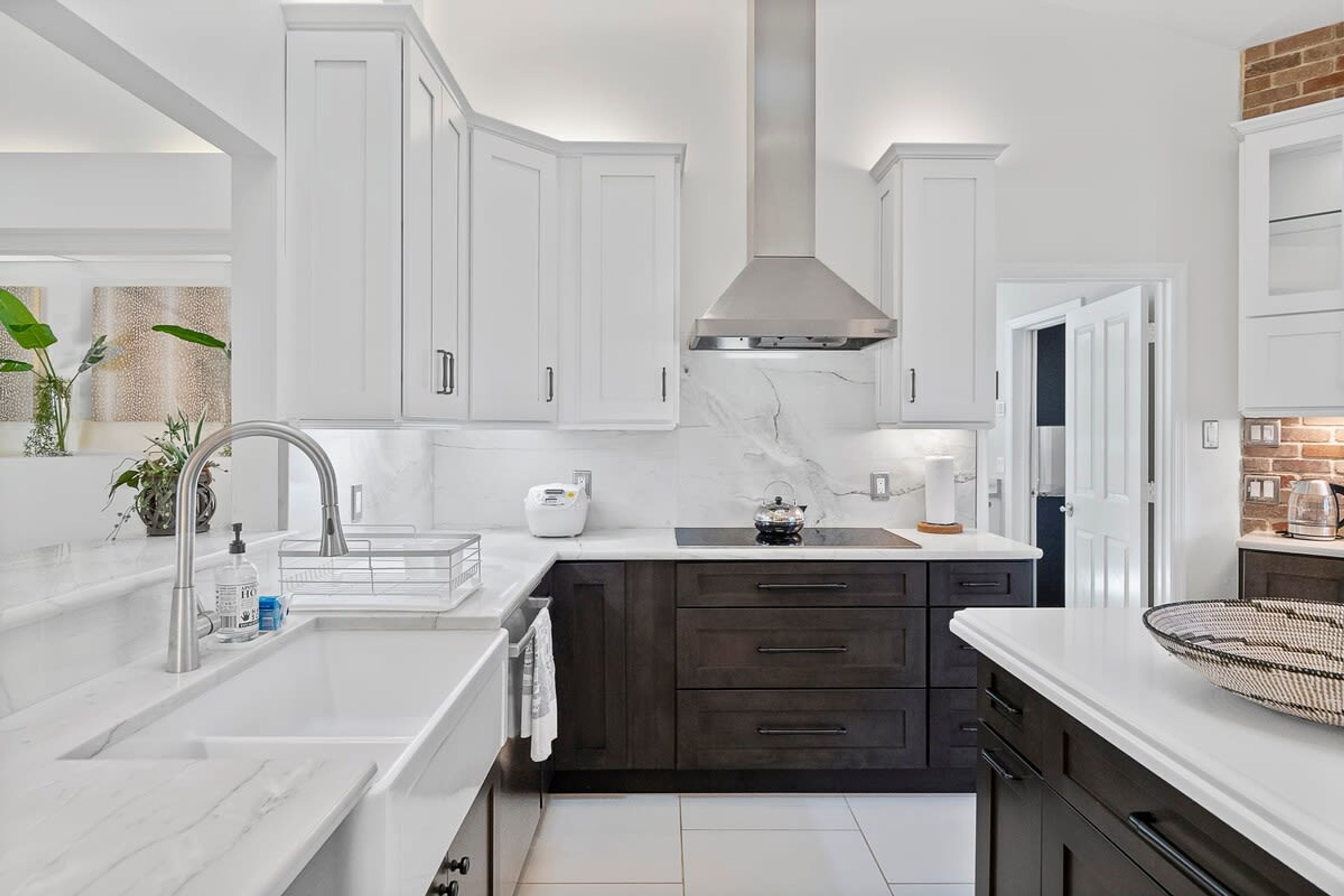 A modern kitchen with white cabinets, dark countertops, a stainless steel range hood, and a marble backsplash.