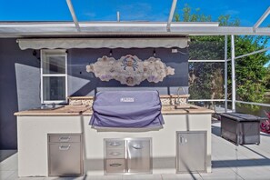 An outdoor kitchen with a grill, a sink, and storage cabinets. - Luxury Heated Pool Home on Saltwater Canal w Tiki (Palm Coast)