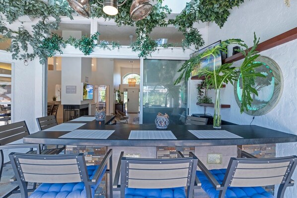 Un espace repas moderne avec un îlot central, des chaises bleues rembourrées et des plantes suspendues.