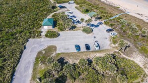 An aerial view of a coastal property with a parking lot, a small building with a green roof, and a beach in the background.