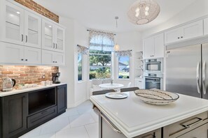 A modern kitchen with white cabinetry, a brick accent wall, and a large island. - Luxury Heated Pool Home on Saltwater Canal w Tiki (Palm Coast)