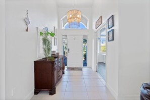 A hallway with a wooden cabinet, a chandelier, and framed artwork on the walls. - Luxury Heated Pool Home on Saltwater Canal w Tiki (Palm Coast)