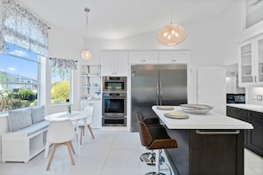 A modern kitchen with white cabinetry, a large stainless steel refrigerator, and a dining area with a white table and chairs.