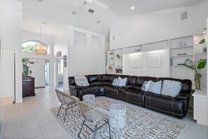 Un salon moderne avec un canapé d’angle en cuir foncé, un tapis à motifs et un mur blanc agrémenté d’étagères.