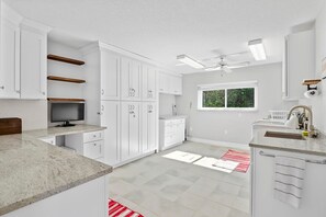 A modern kitchen with white cabinets, a granite countertop, and a window with a view of greenery. - Luxury Heated Pool Home on Saltwater Canal w Tiki (Palm Coast)