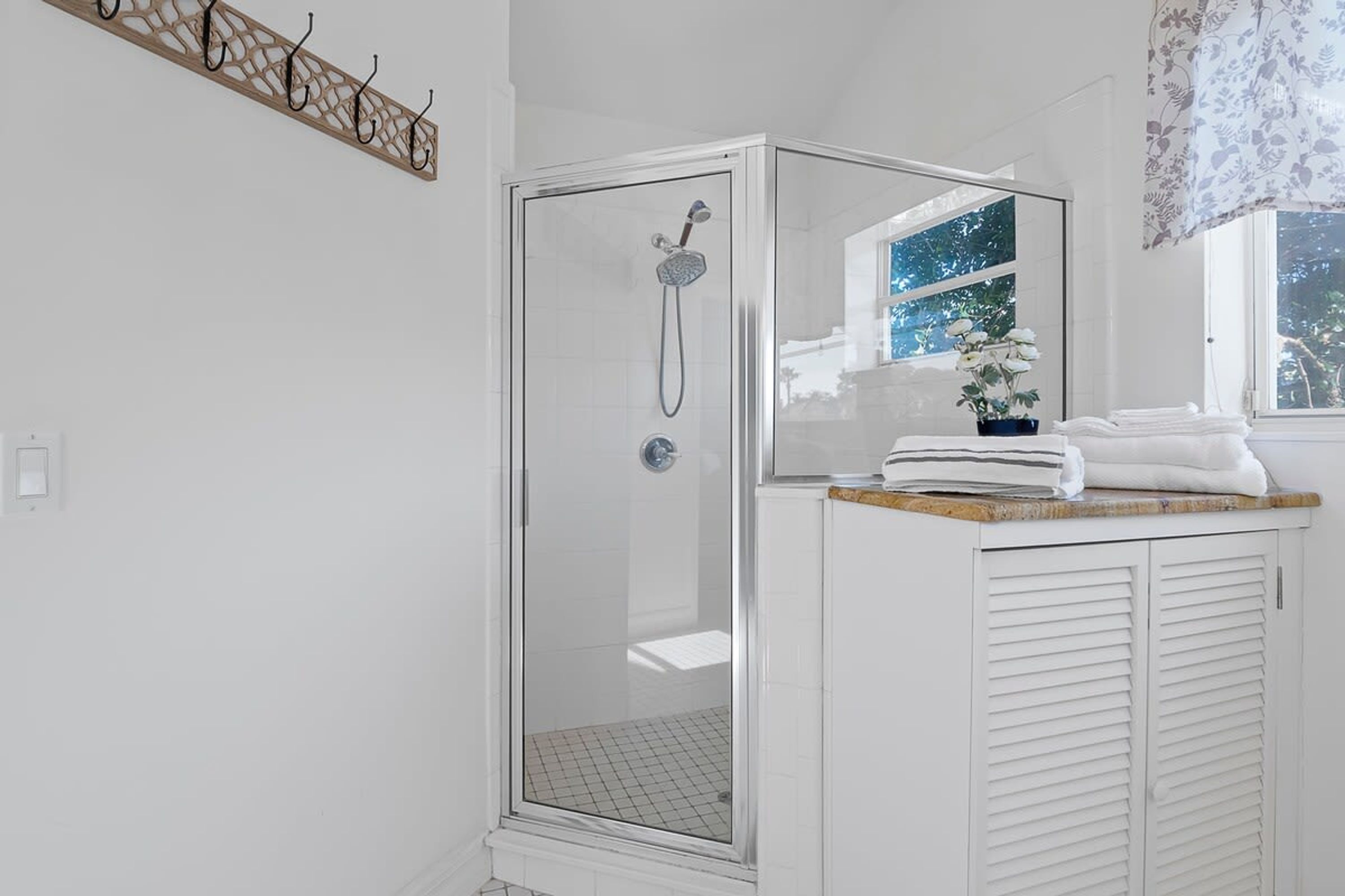A modern bathroom with a glass-enclosed shower, a white vanity with a mirror, and a window with a view of trees.
